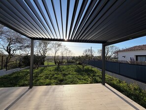 Área externa coberta com vista para um jardim e um edifício ao fundo.