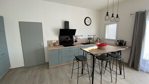 A modern kitchen with a wooden countertop, a built-in oven, and a coffee machine. There are bar stools and a dining table with a red basket on it. - Villa Climatisée Proche Centre (Uzès)