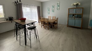 A dining area with a wooden table and chairs, a kitchen area with a red basket, and a blue cabinet. - Villa Climatisée Proche Centre (Uzès)