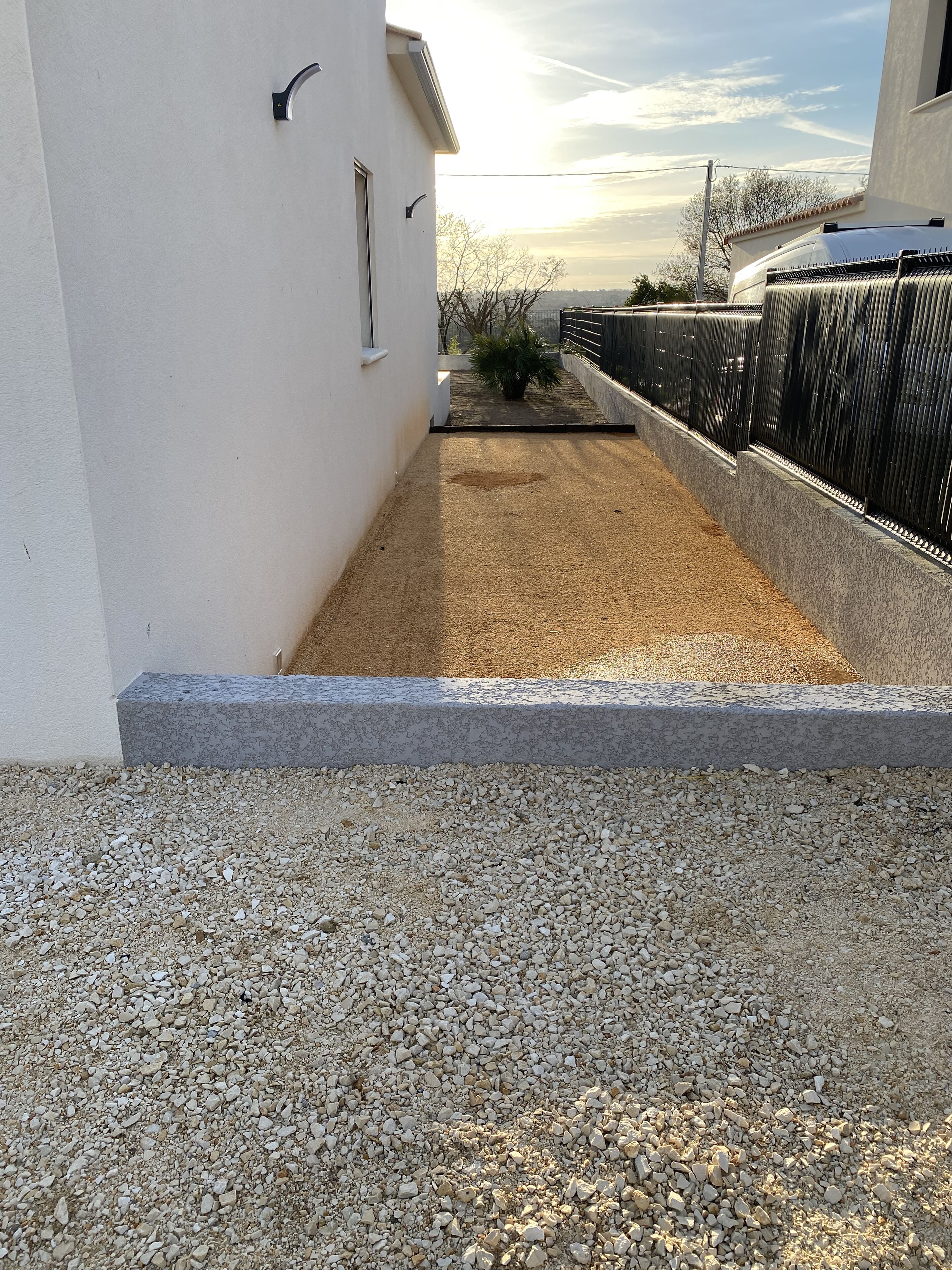 Ein Kiesweg führt zu einem weißen Gebäude mit einem kleinen Garten.