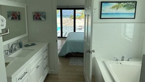 A modern bathroom with a large bathtub, a vanity with a mirror, and a view of a beach through an open door. - BRAND NEW Beachfront Villa best sandy beach in TCI with pool Fox Tail Palm Villa (Whitby)