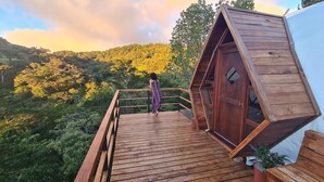 A wooden deck with a railing leading to a cabin with a sloped roof. - Naturave #1 Into the woods, 1 (Monte Verde)