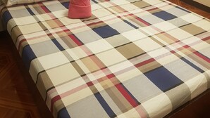 Una cama con colcha y almohadas a cuadros, suelo de madera y pared lisa.