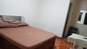 Habitación individual con cama, piso de madera, una mesita con silla y un armario.