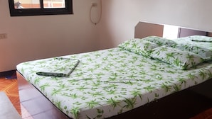 Una cama individual con estampado de hojas verdes, una mesita pequeña y una ventana con vistas al exterior.