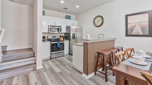 A modern kitchen with white cabinets, stainless steel appliances, and a wooden island with stools. - Amazing 3Bdr House near Disney 16106 (Osceola County)