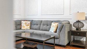 A grey sofa with patterned cushions, a dark coffee table, and a lamp on a side table. - Your VIP Home near Disney! (Osceola County)