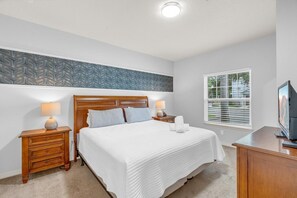 A bedroom with a bed, two bedside tables with lamps, a television, and a window with blinds. - Your VIP Home near Disney! (Osceola County)