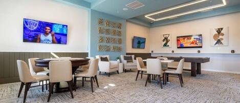 A conference room with a pool table, multiple chairs, and a TV screen displaying a sports event.