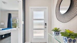 A hotel room with a bed, a window with curtains, a door with frosted glass panels, and a wall-mounted mirror. - Outstanding 5BDR Disney Vacation (Kissimmee)