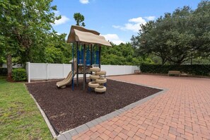 A playground with a slide and climbing structure, surrounded by a brick pathway and greenery. - Your Disney Vacation Home! (Osceola County)