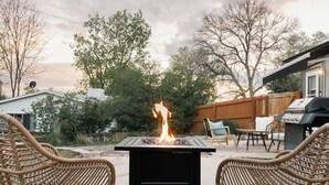Un patio trasero con un hogar, sillas de mimbre y una parrilla.