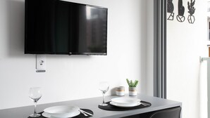 A modern dining area with a flat-screen TV mounted on the wall, a table set with plates, glasses, and a small plant. - Studio On Imarés Moema (São Paulo)