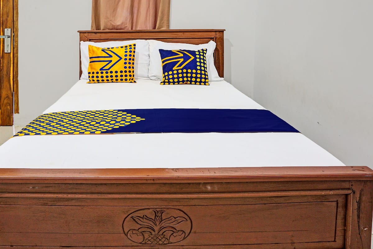 A bed with a wooden headboard, white bedding, and two pillows with yellow and blue patterns.