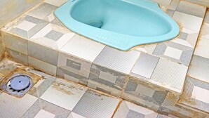 Un baño con inodoro azul, piso de baldosas y desagüe.