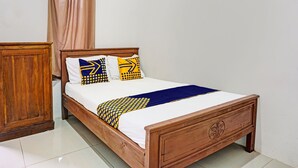 Una cama de madera con un colchón blanco, almohadas estampadas en azul y amarillo, y una manta de color azul.