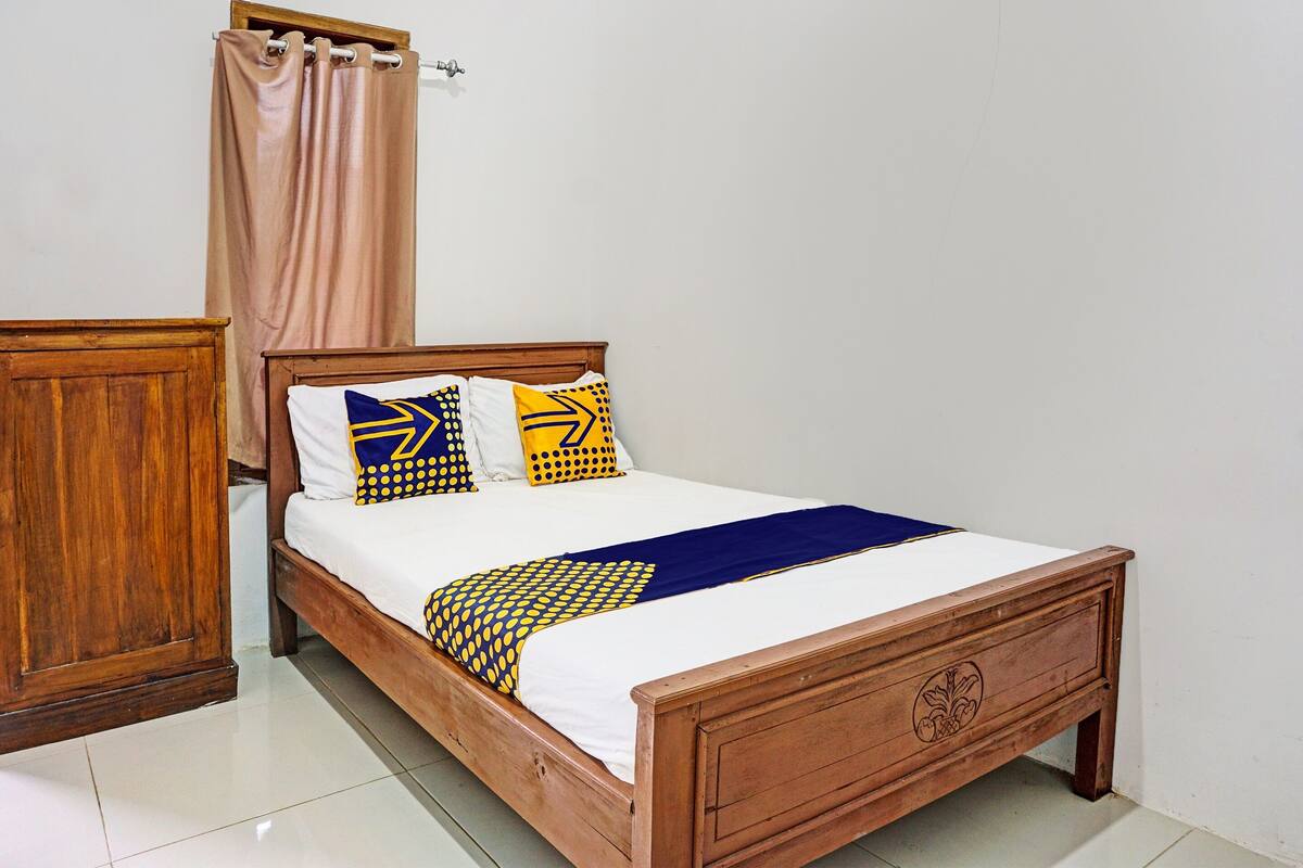 A wooden bed with a white mattress, blue and yellow patterned pillows, and a blue throw blanket.