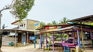 Una pequeña tienda a la vera de la carretera, con un letrero, una motocicleta estacionada afuera y un árbol al fondo.
