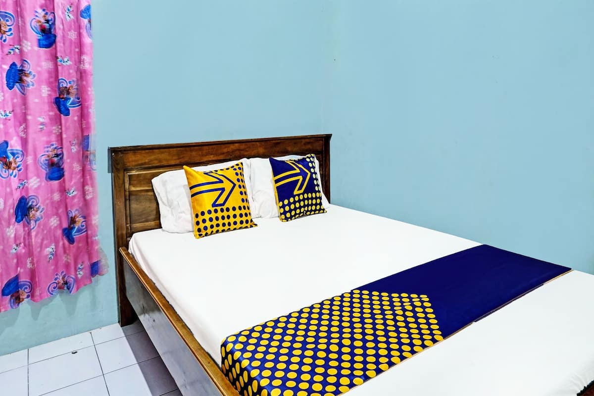 A bed with a white mattress, two pillows with yellow and blue patterns, and a blue and yellow polka dot blanket.