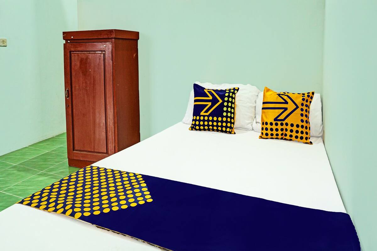 A room with a bed, two pillows with arrow designs, a wooden wardrobe, and a green tiled floor.
