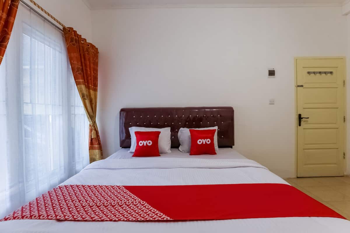 A hotel room with a bed, two red pillows with "OYO" text, a white and red patterned bedspread, and a yellow door.