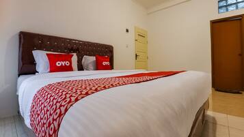 A neatly made bed with a patterned bedspread and pillows, a wooden headboard, and a door in the background.