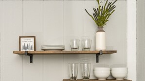 A kitchen with white cabinets, stainless steel appliances, and wooden shelves holding dishes and glasses.