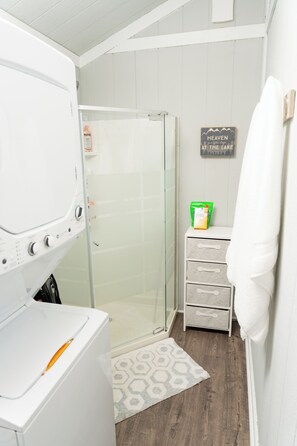 A laundry area with a washing machine, a glass shower enclosure, and a towel rack.