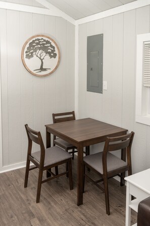 A dining area with a wooden table and four chairs, a wall-mounted electrical panel, and a window with blinds.