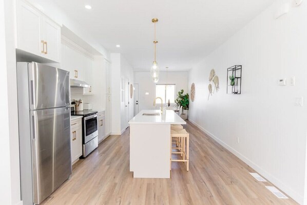 A modern kitchen with stainless steel appliances, a central island, and wooden flooring.