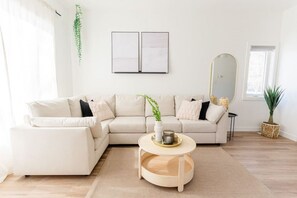 Uma sala de estar moderna com um sofá seccional bege, uma mesa de centro redonda e um espelho grande.