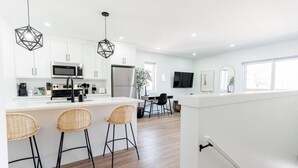Une cuisine moderne avec des meubles blancs, un îlot central doté de tabourets, un four à micro-ondes et un réfrigérateur.