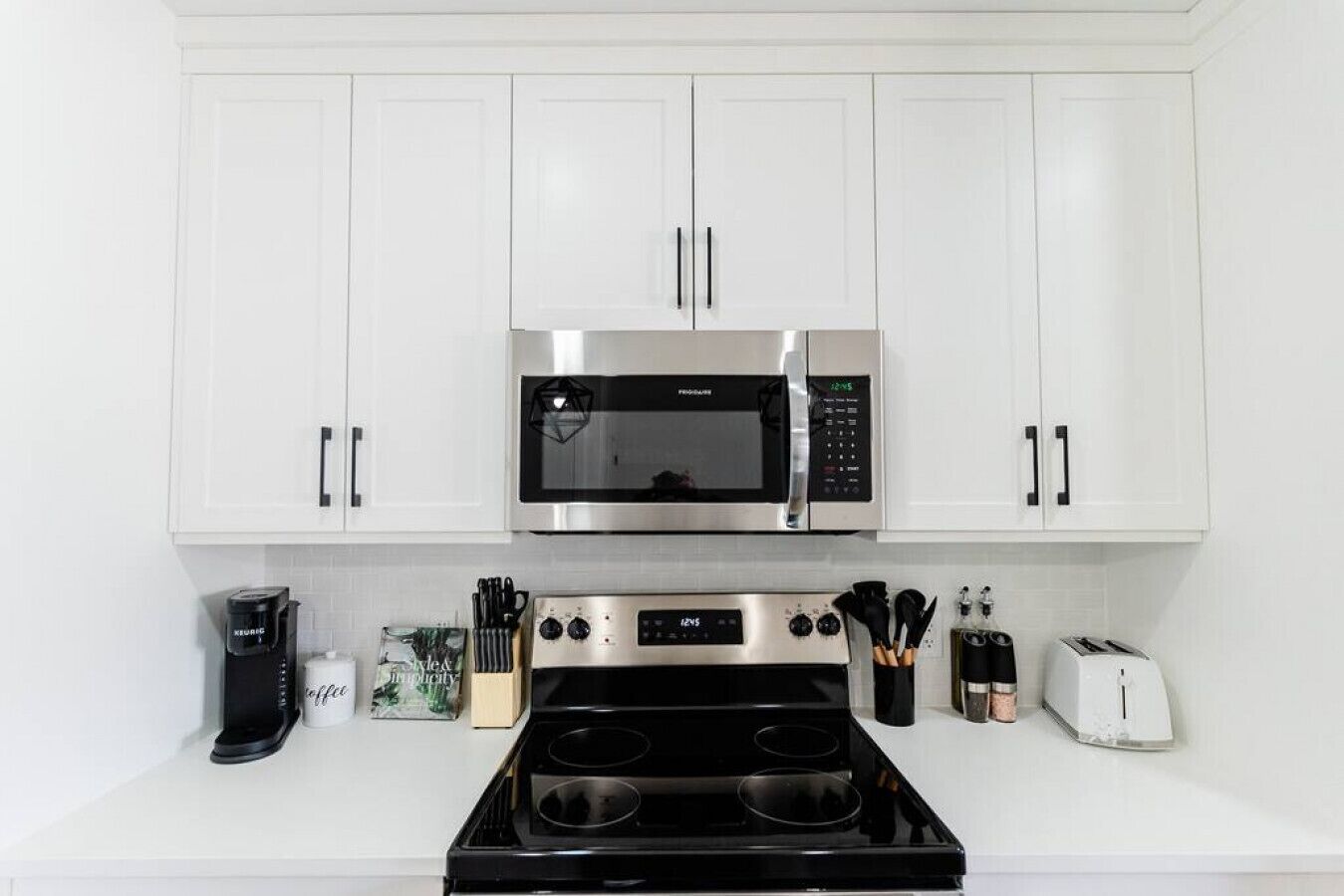 A kitchen with white cabinets, a stainless steel microwave, a stove, a coffee maker, and a toaster.