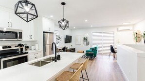 Une cuisine moderne avec des meubles blancs, des appareils en acier inoxydable, un îlot central doté de tabourets et des luminaires suspendus aux formes géométriques.