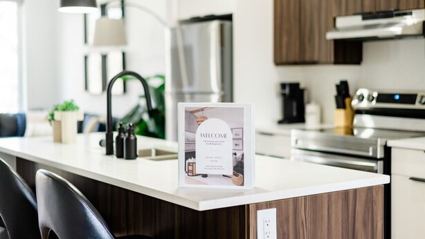 Una cocina moderna con encimera blanca, electrodomésticos de acero inoxidable y un cartel de bienvenida.