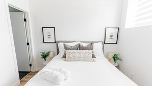 A neatly made bed with white linens and a folded towel, two bedside tables with lamps and plants, and a framed picture on the wall. - *1min Riverview Health 7min Downtown  Free Parking (Winnipeg)