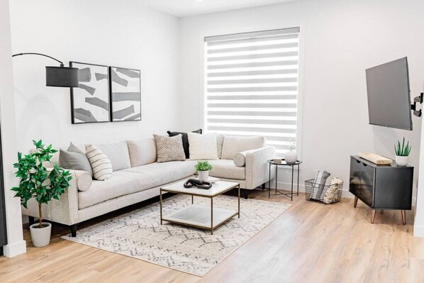 A modern living room with a sectional sofa, a coffee table, a small side table, a potted plant, and a TV on a stand.