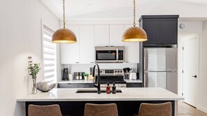 A modern kitchen with a central island, two pendant lights, and a refrigerator. - Riverview Health | Trendy Area | Free Parking (Winnipeg)