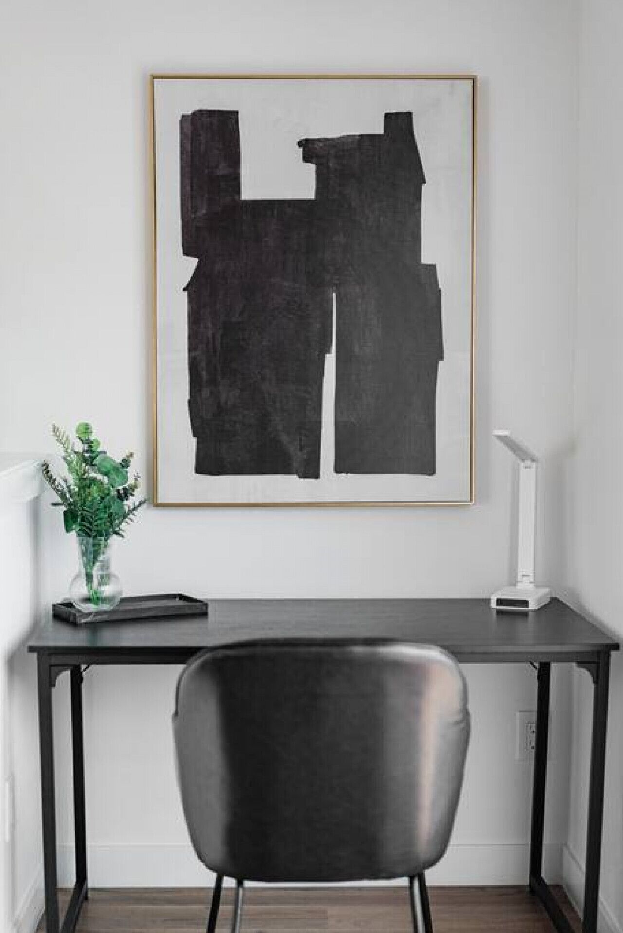Et moderne arbejdsområde med et skrivebord, stol og et indrammet abstrakt billede.