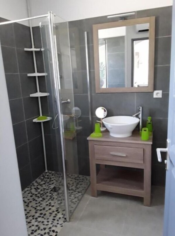 A bathroom with a glass shower enclosure, a sink, and a mirror.