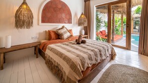 Une chambre avec un grand lit, deux lampes de chevet, un banc, une grande fenêtre et une vue sur une piscine.