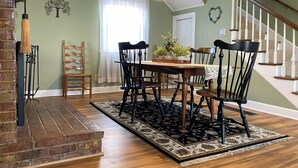 A dining area with a wooden table, black chairs, a chandelier, and a brick fireplace. - Happy Moo's Fink Family Farm, where cows & guests are free to enjoy our 50 acres (Versailles)