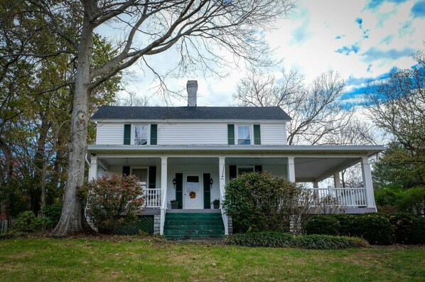 A two-story house with a porch, a chimney, and a front door. - Happy Moo's Fink Family Farm, where cows & guests are free to enjoy our 50 acres (Versailles)