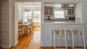 Une cuisine moderne avec des meubles blancs, un îlot central doté de tabourets de bar et un coin repas avec des meubles en bois.