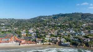 Vue aérienne d’une ville côtière avec une plage, des immeubles résidentiels et un paysage vallonné en arrière-plan.