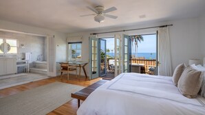 Une chambre avec un grand lit, un bureau et une chaise, une salle de bain avec un miroir et un lavabo, et un balcon avec vue sur l’océan.