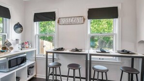 A kitchen with a white countertop, a coffee machine, and a microwave. There are four stools and a decorative sign on the wall. - Shocker Shack - 2K - Near WSU, Park - Fenced Yard (Wichita)