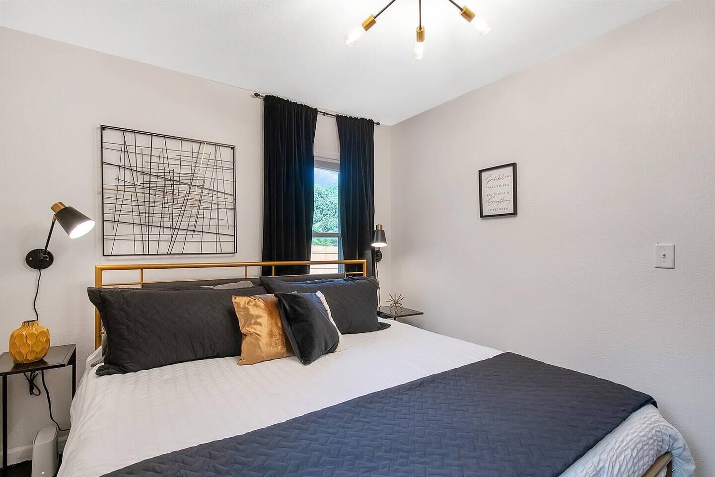 A neatly arranged bedroom with a bed, bedside lamps, a wall art piece, and a framed quote on the wall.