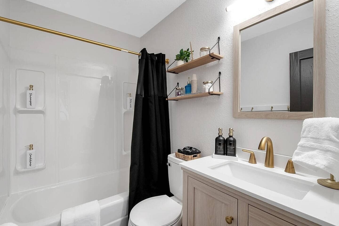 A modern bathroom with a white vanity, gold fixtures, and a black shower curtain.