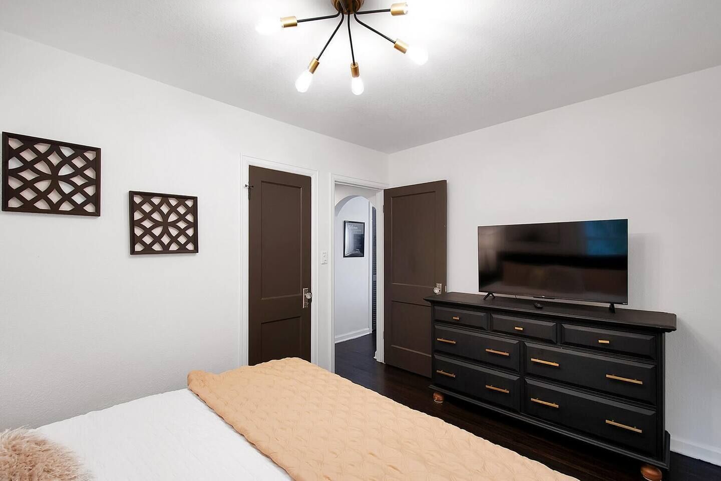 Un dormitorio con una cama, un televisor sobre un tocador y una puerta que da a otra habitación.